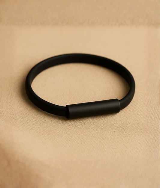 Minimalist black silicone and stainless steel bracelet displayed on a beige surface, showcasing its smooth matte finish and sleek design.