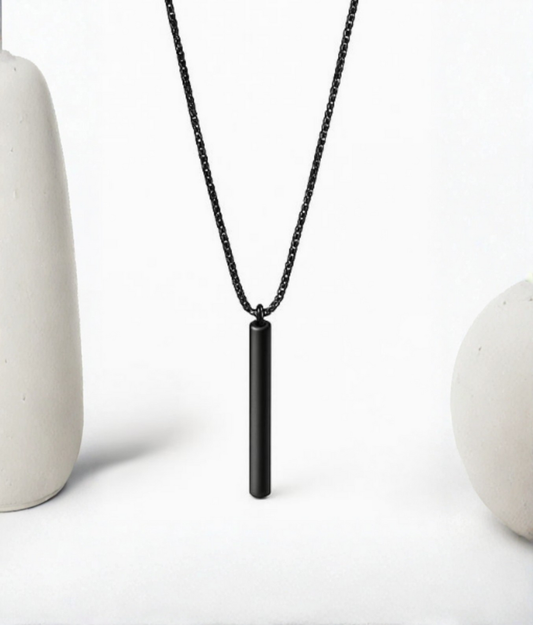 Minimalist matte black pendant necklace displayed between smooth white ceramic shapes, highlighting its sleek and modern design.