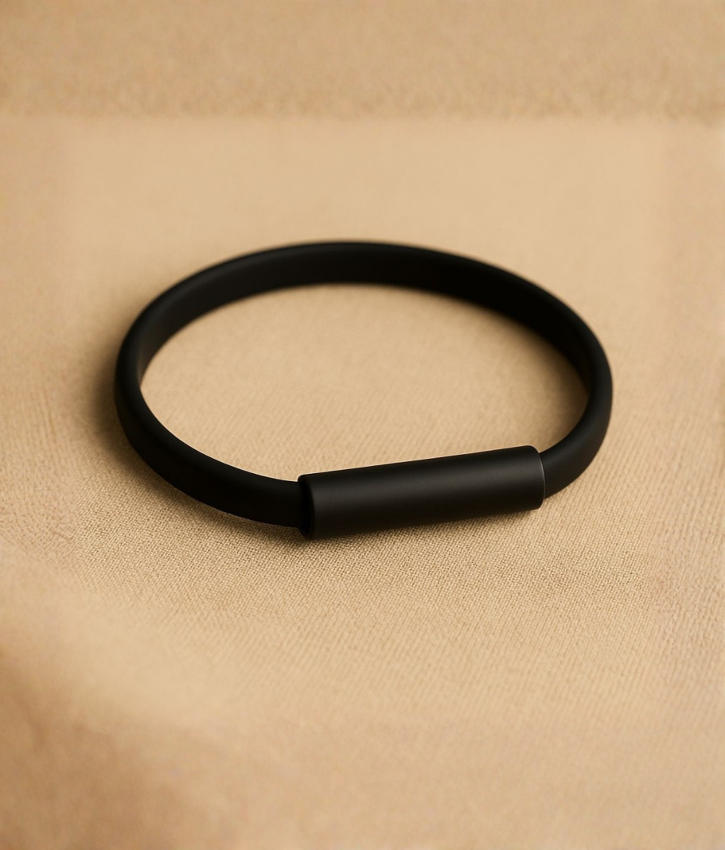 Minimalist black silicone and stainless steel bracelet displayed on a beige surface, showcasing its smooth matte finish and sleek design.