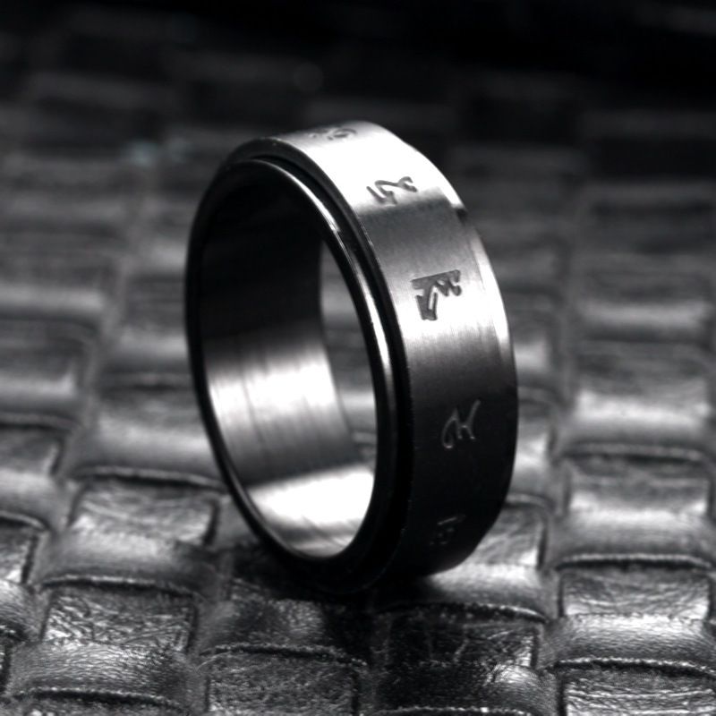Matte black stainless steel ring with engraved minimalist symbols, displayed on a textured dark surface.